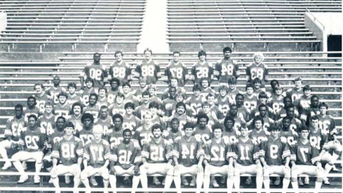 Black and white photo of football team sitting down.